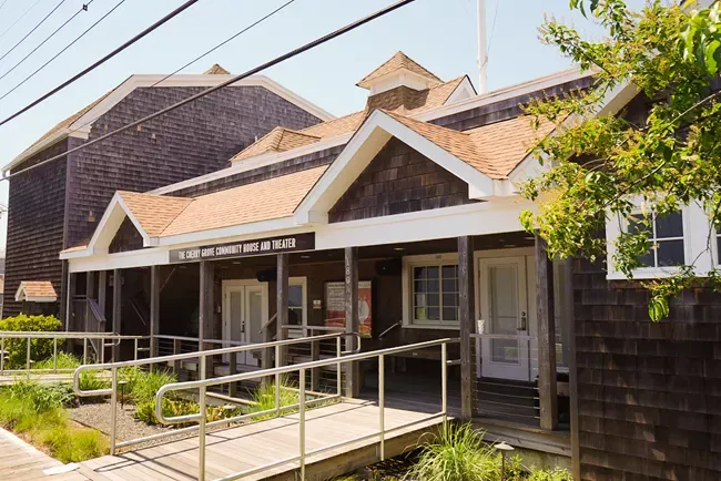 The front of the Cherry Grove Community House and Theatre, which is building brown wooden siding and a reddish brown roof.